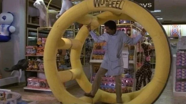 Jack Brown (played by Richard Pryor) stands in a large yellow wheel in the film The Toy.