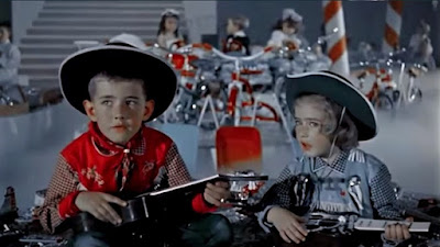 Two children in cowboy-inspired outfits sit, surrounded by toys and giant candy canes. In the background, three other children sit surrounded by bicycles.