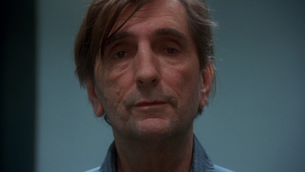 Harry Dean Stanton, a white man with wispy brown hair, looks at the camera with a weary expression.
