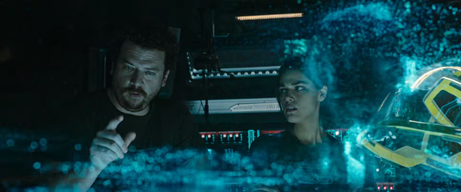 A man with short hair and facial hair points at a futuristic-looking hologram map of stars. A woman stands to his right, looking skeptical.
