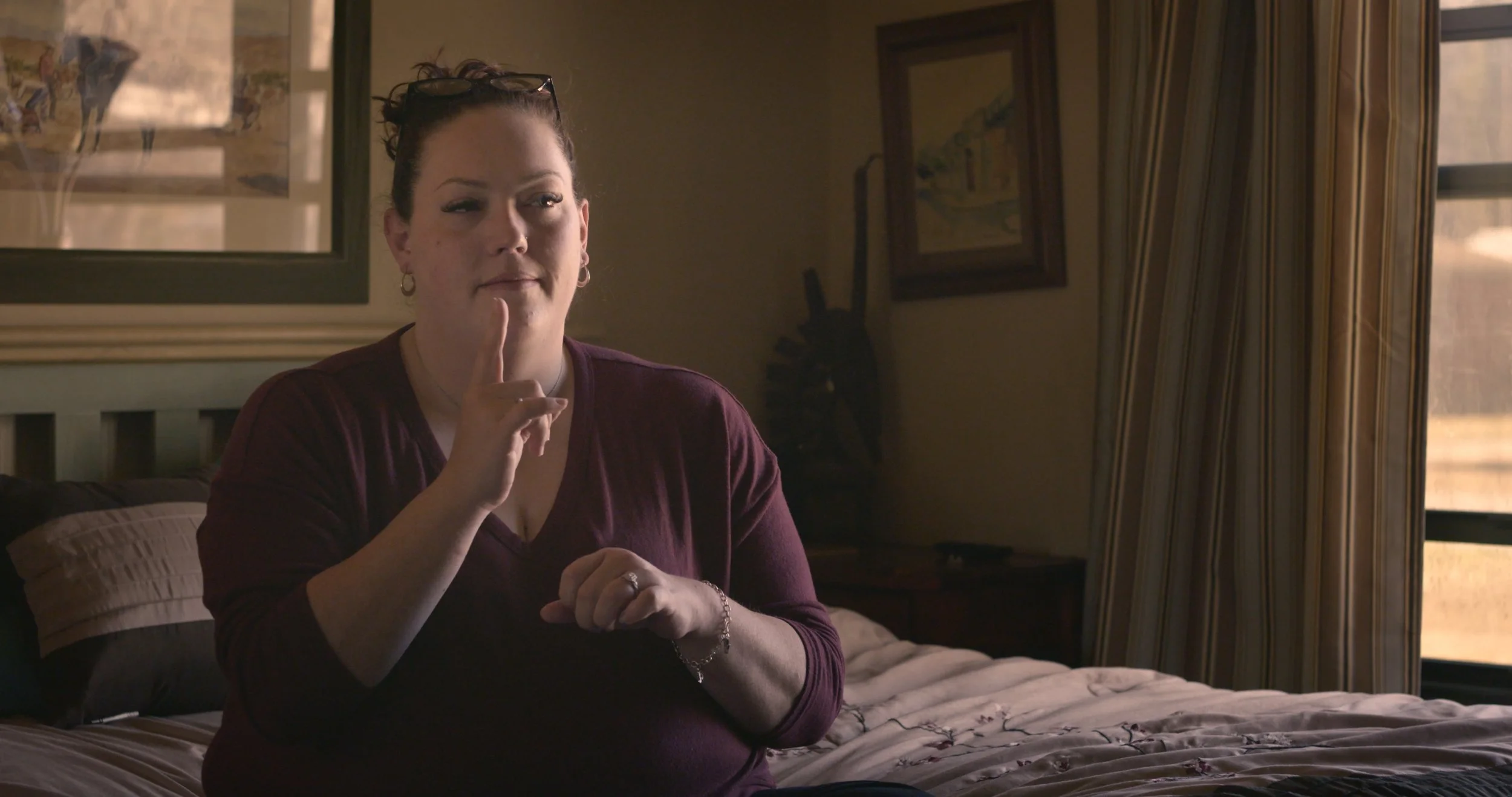 Leslie Estes sits on a bed and signs to the camera.
