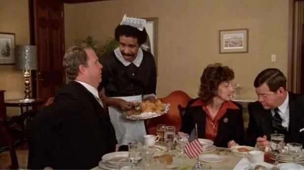 Jack (Richard Pryor) wears a french maid's uniform while serving food to people in a dining room.