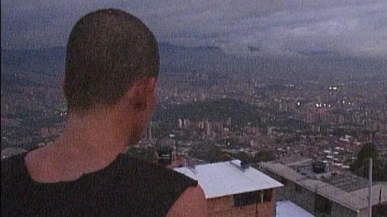 One of the youths in the group looks over the cityscape of Barrio Sagrado while standing on a rooftop in the film Barrio Triste.