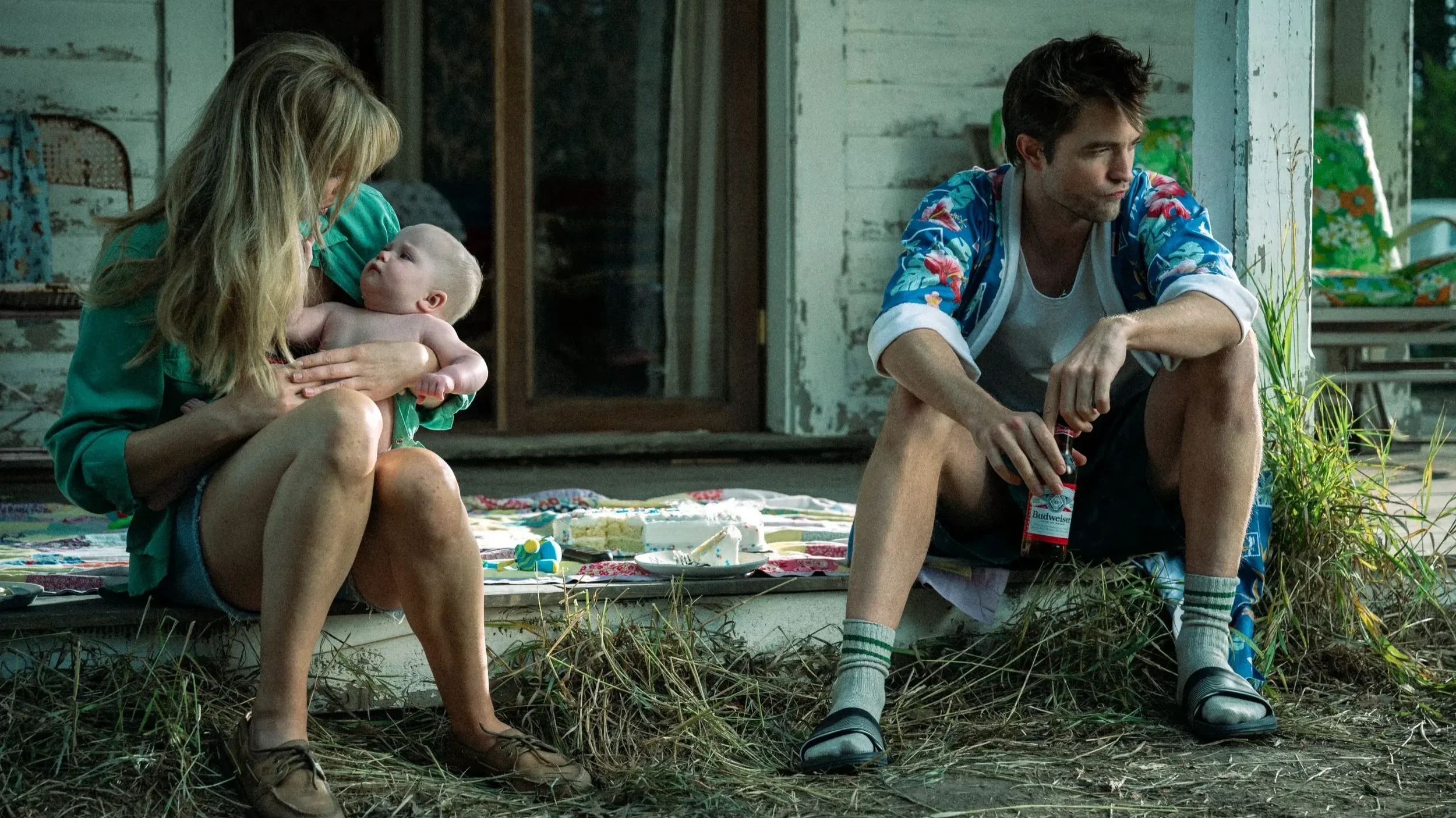 Jennifer Lawrence holds a baby while sitting on a porch with Robert Pattinson in 'Die My Love.'