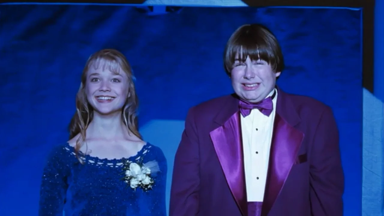 Ariana Richards gives a big grin in a blue prom dress as Melissa Lefevre, as she stands beside a purple suit wearing Angus (played by Charlie Talbert) in the film, 'Angus.'