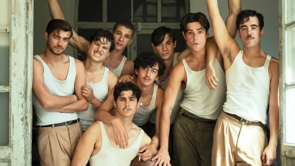 The cast of the film La bola negra poses in white tanks in front of a dirty, white barn door.