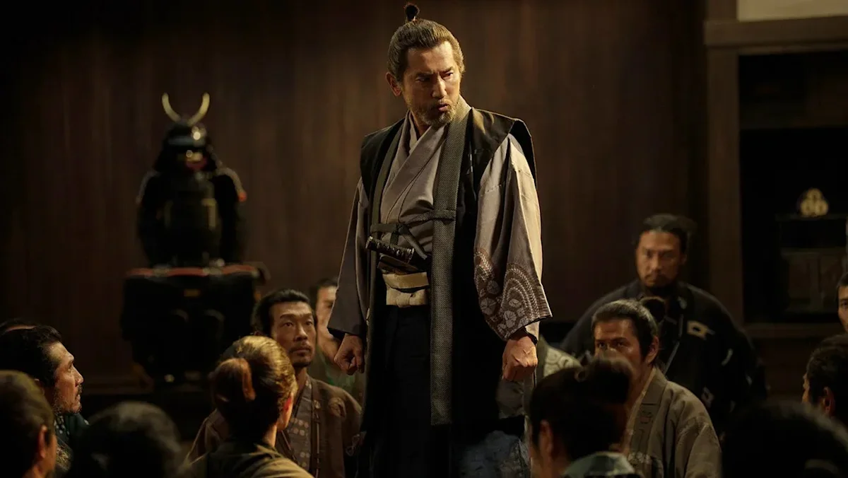 Lord Araki Murashige stands in the middle of a seated group of his men and addresses them.