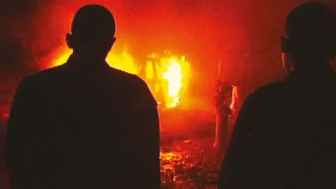 Two unseen people look at a structure on fire in the film Barrio Triste.