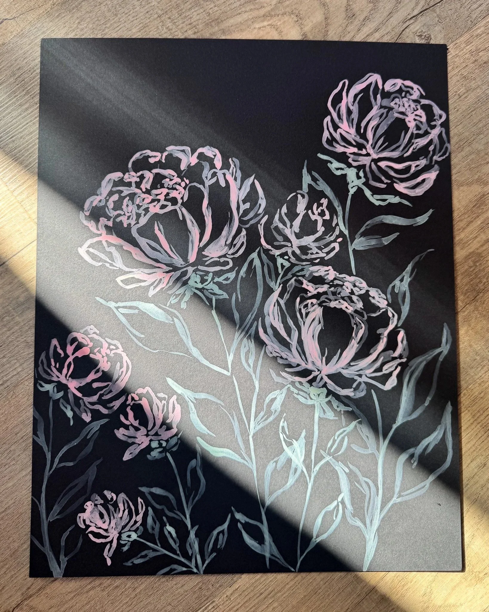Floral painting on black paper in a beam of sunlight