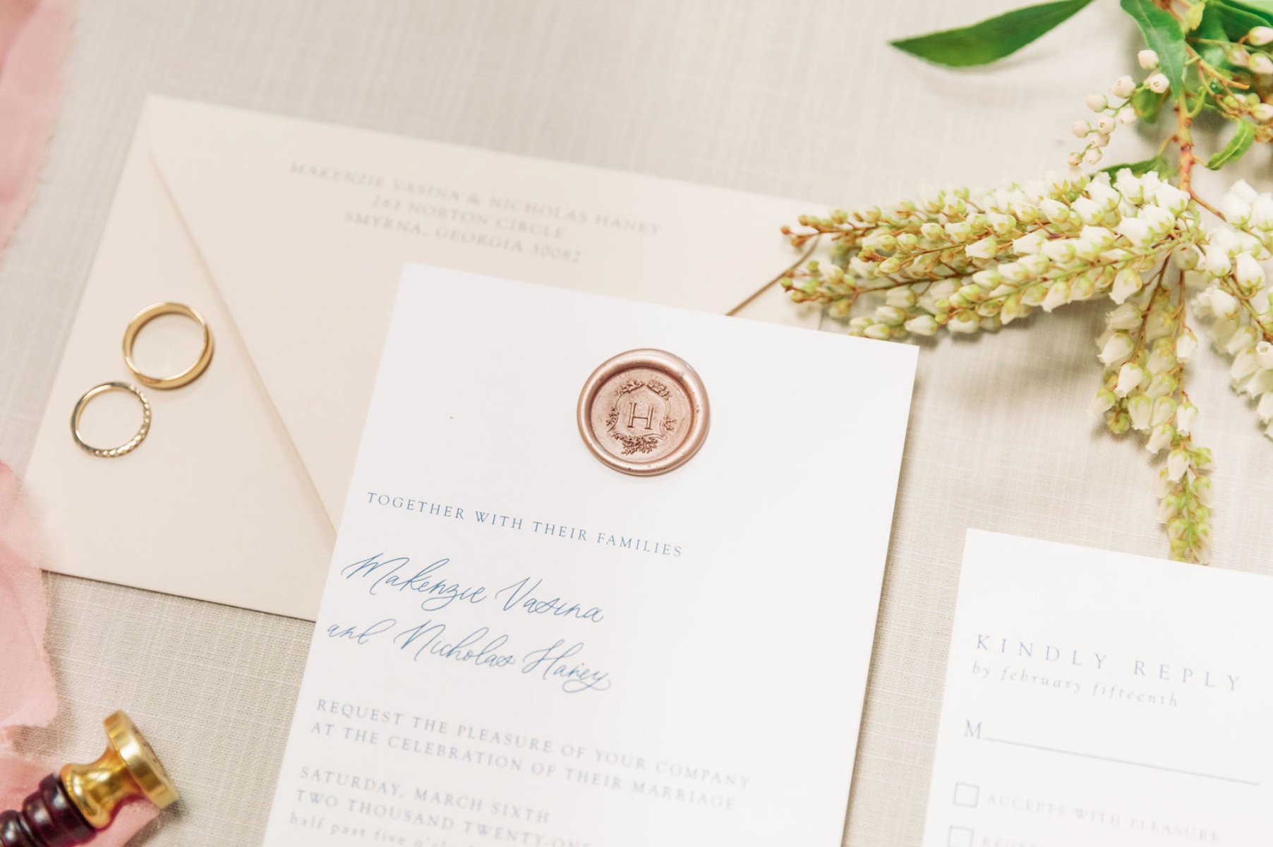 Wedding invitation with a rose gold wax seal, two rings, and floral decorations.