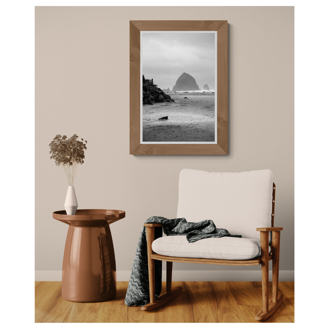 Black and White Coast at Haystack Rock Cannon Beach fine art print framed in wood on a neutral wall with chair and accessories, Britt Vasina Studio