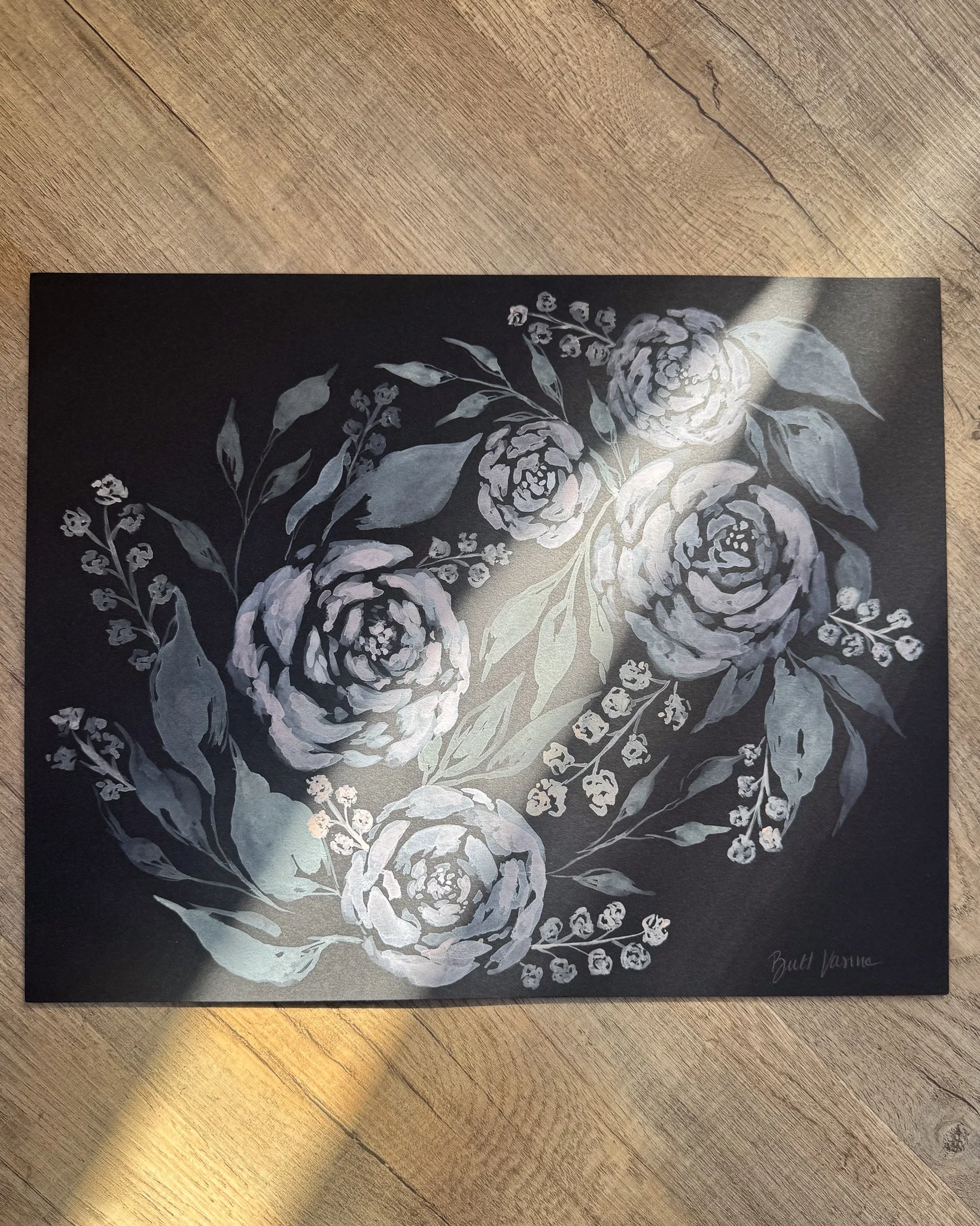 Floral painting on black paper in a beam of sunlight