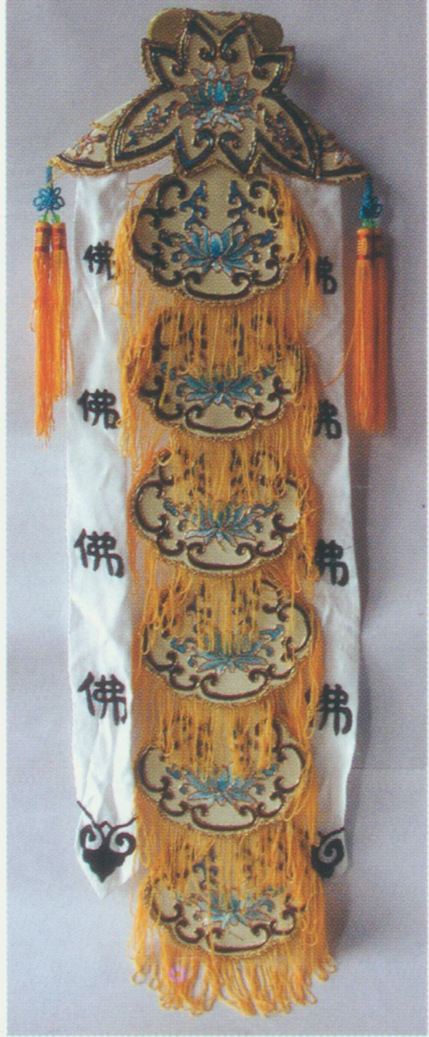 Taoist Priestess Scarf A soft hat, also known as “Miaochang Scarf” for it is worn by Chen Miaochang, a character in The Jade Hairpin . The top is made of two ladder-shaped satin cloths. A pair of ribbons embroidered with the word “Buddhism” in Chinese is attached to the hat on both sides. The back consists of six light yellow or white oval cloths, with the word “Buddhism” in Chinese at the center. The hat is decorated with yellow bullion fringes and two shorter ribbons at bottom. It is worn by Taoist priestess, hence the name.