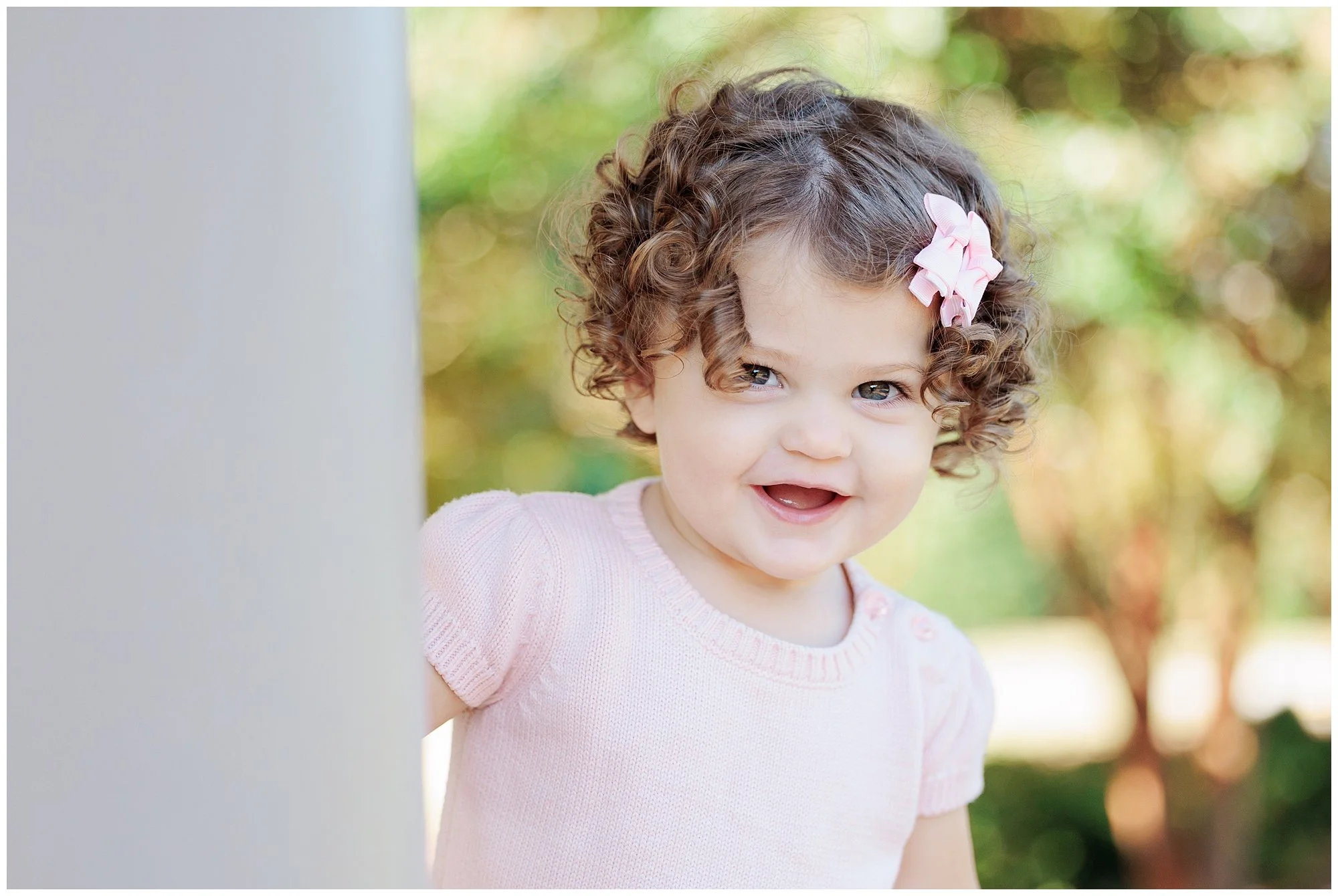 little girl in pink dress peaking around column