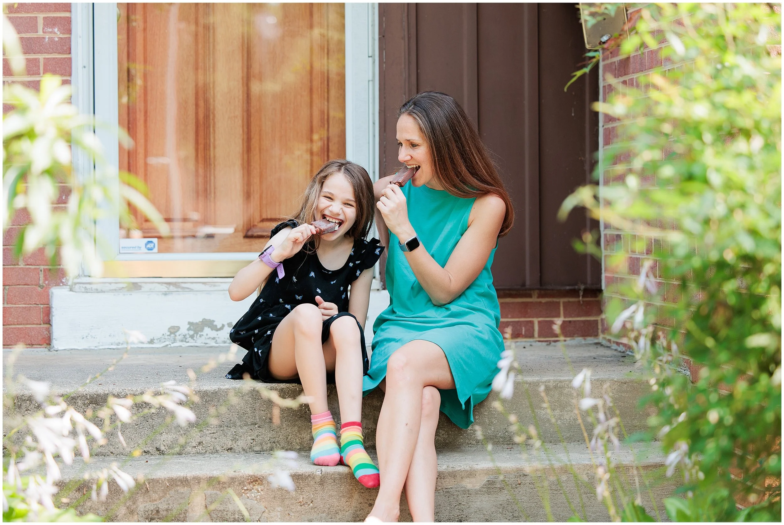 mother and daughter laughing and eating popsicles on porch
