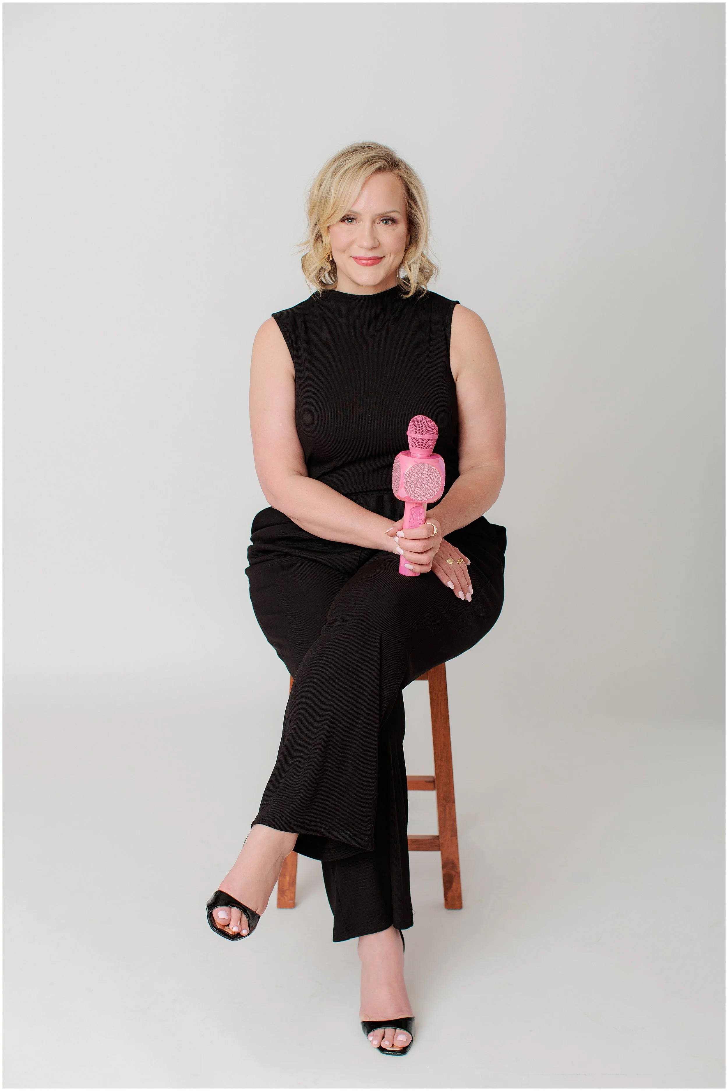 brand photo of female entrepreneur sitting on stool holding pink microphone
