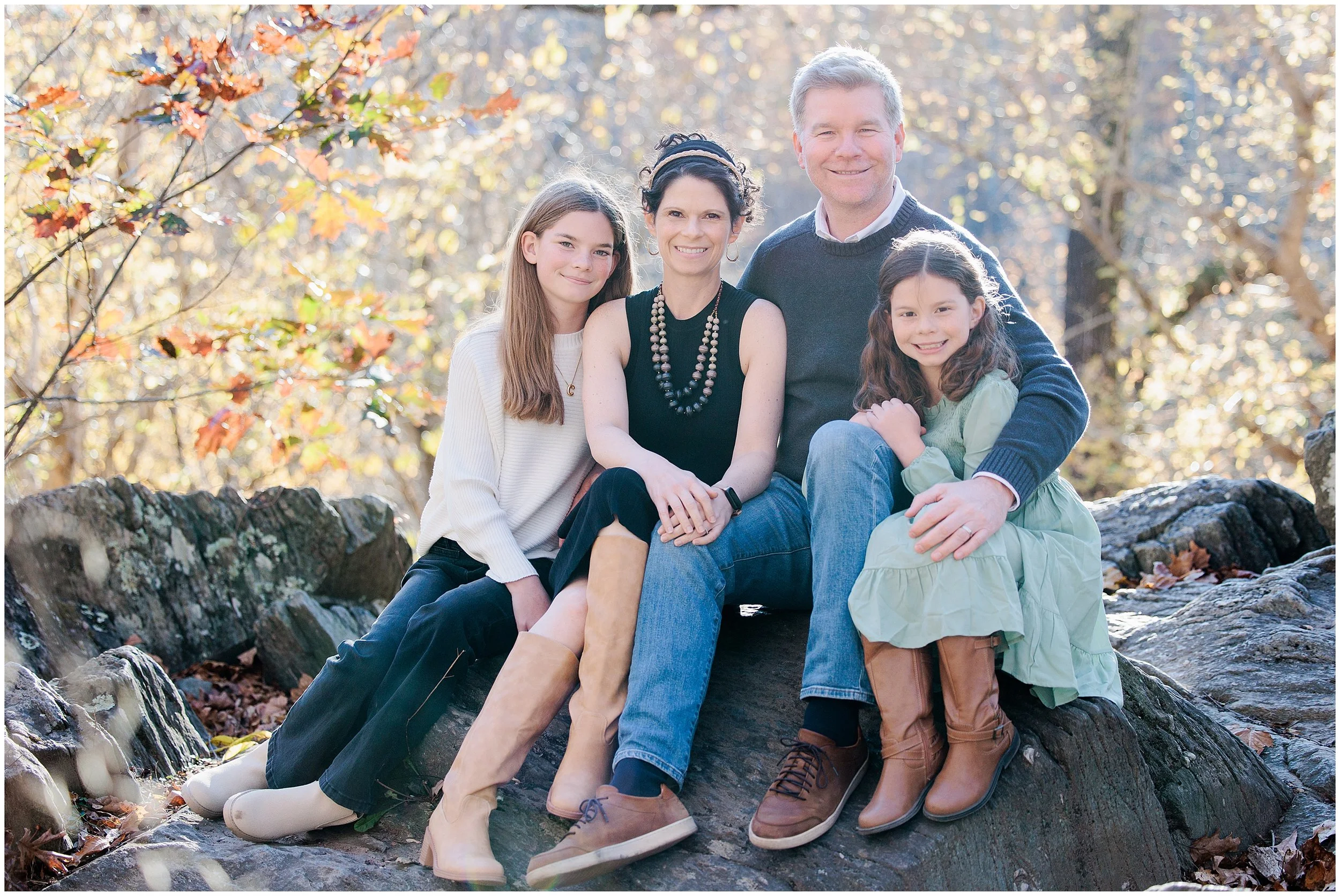 family sitting on rock in fall foliage in Maryland