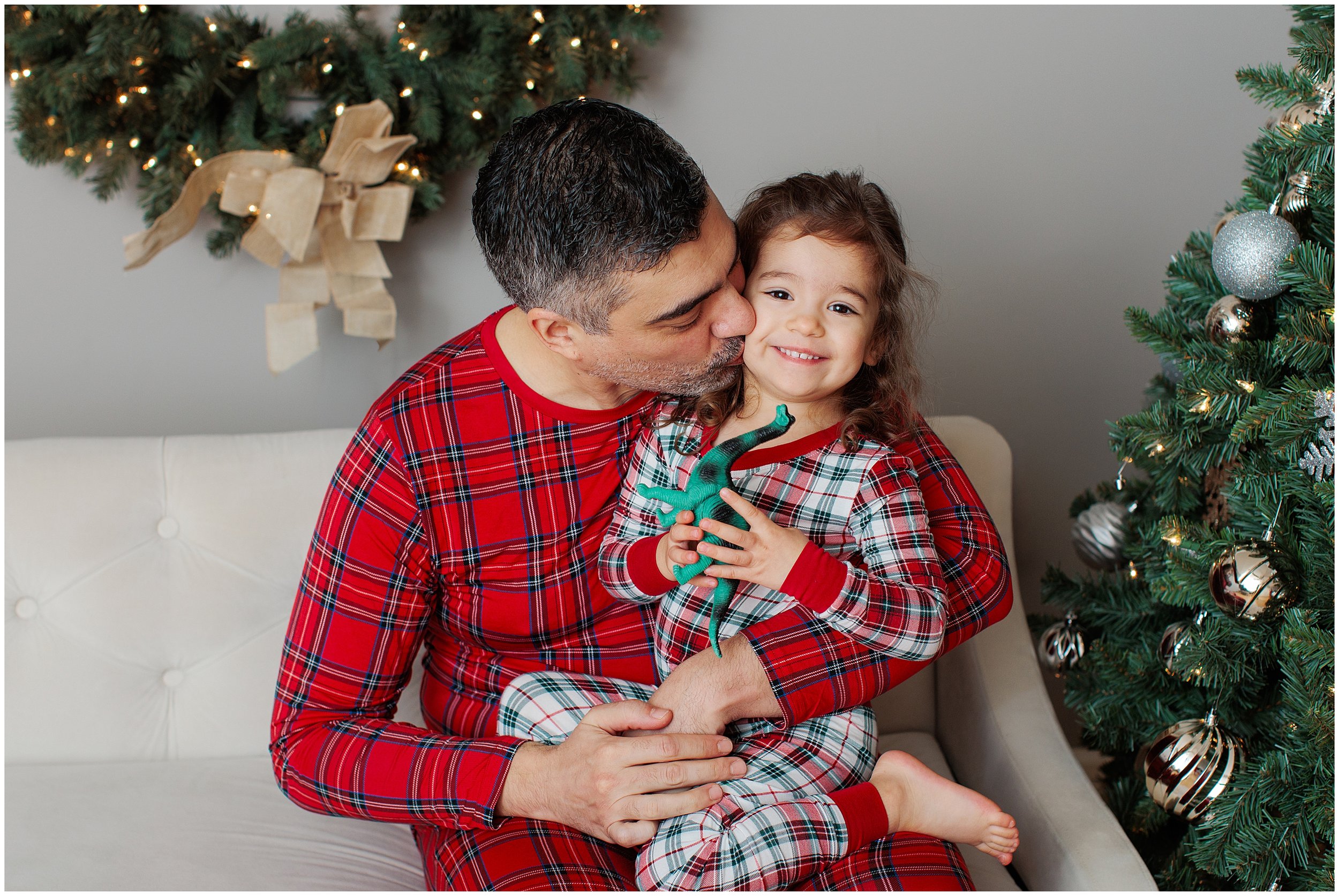 Little girl sitting on dad's lap with a Christmas backdrop