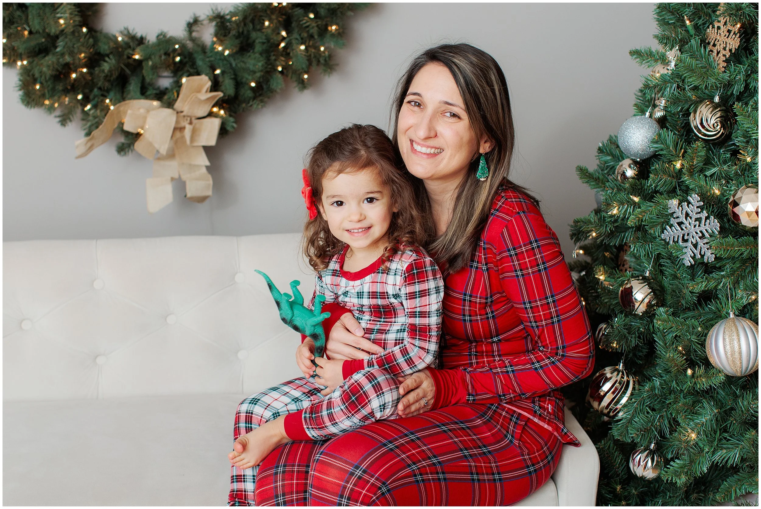 Three year old girl sitting on mom's lap in Christmas PJs by the Christmas tree