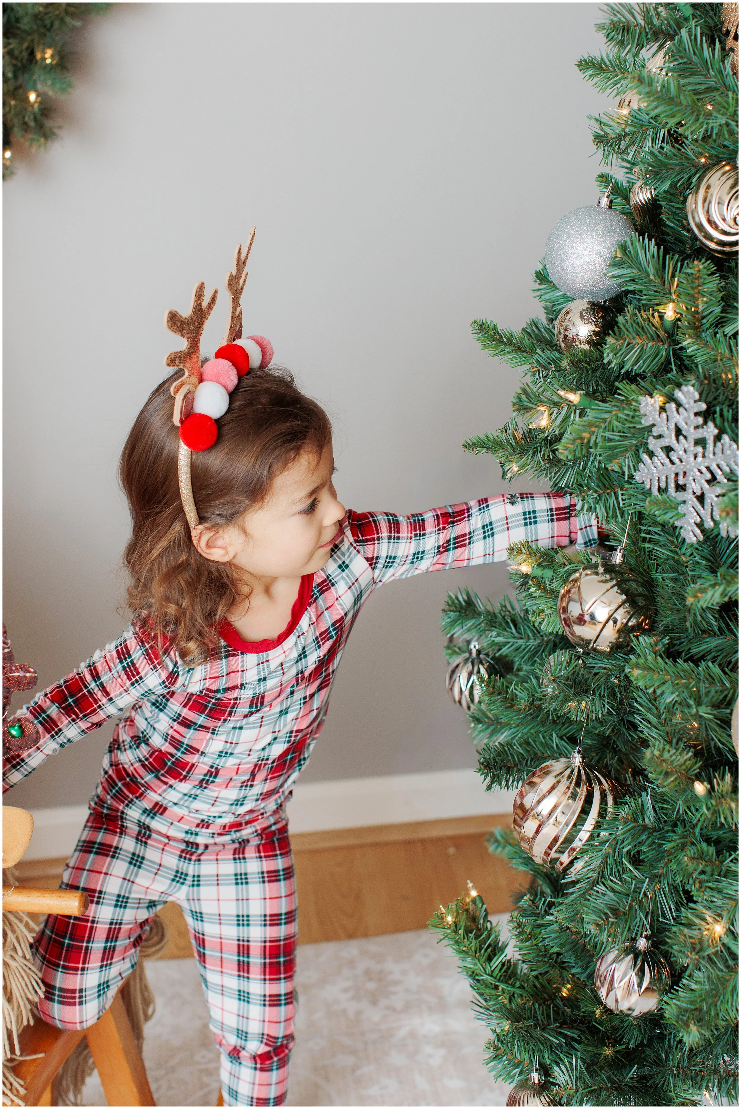 3 year old girl looking at Christmas ornaments on a Christmas tree in her pajamas