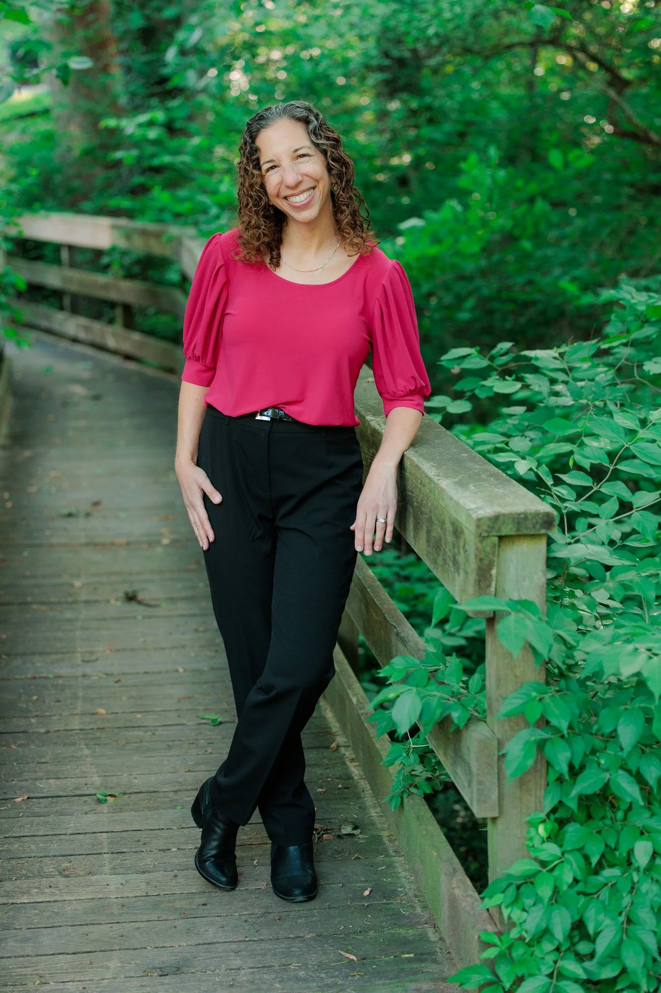  outdoor therapist standing on a bridge and smiling in a pink top 