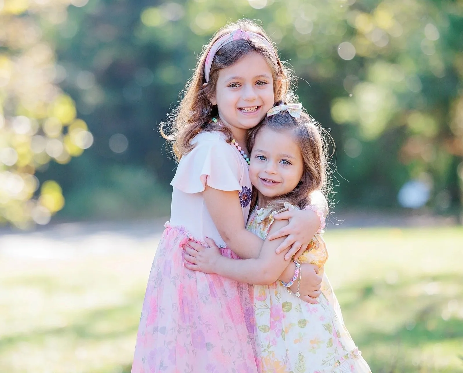 2 young sisters hugging each other in park during a family photo session in Arlington, VA