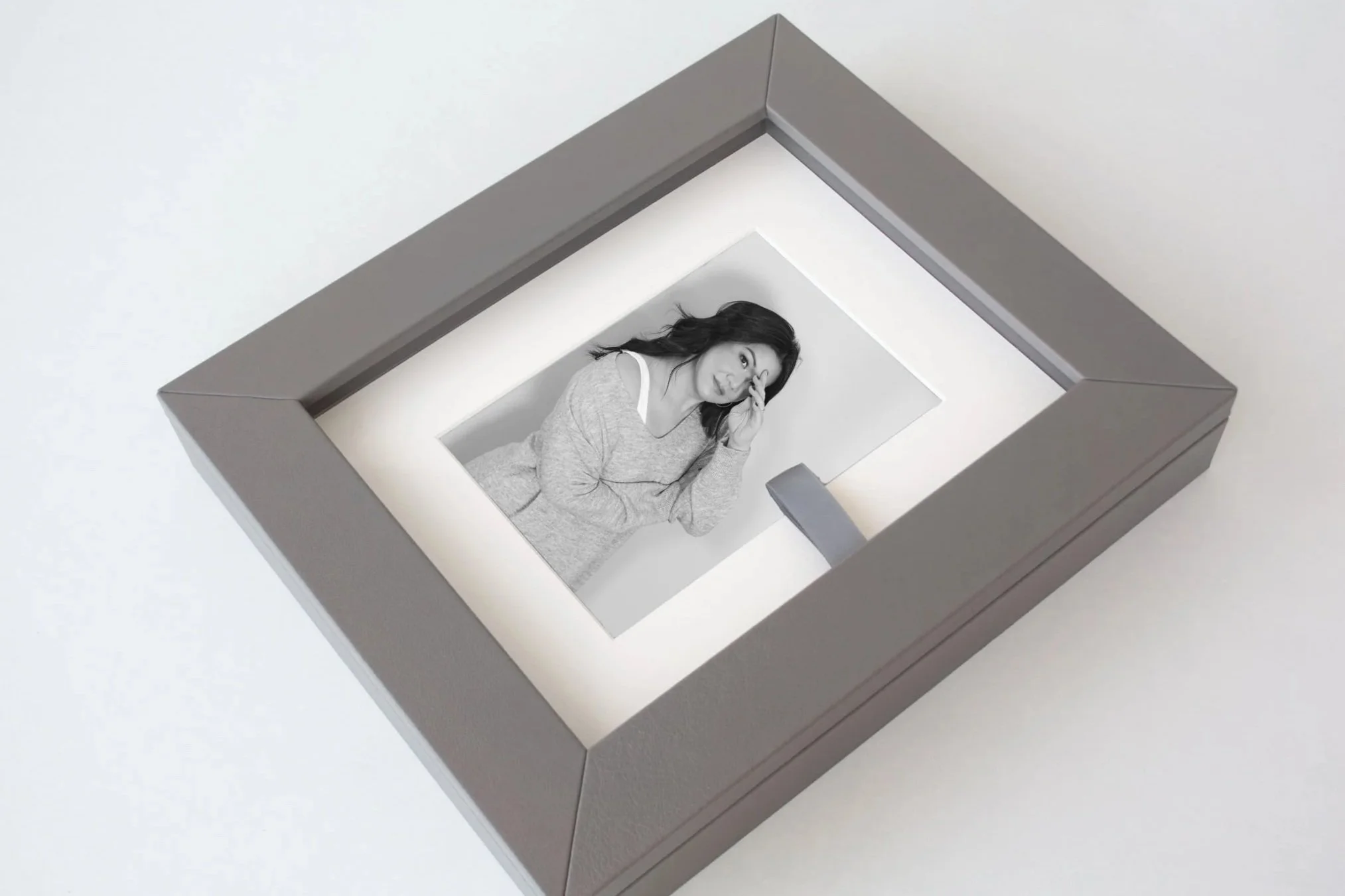 A black and white photo of a woman looking through a rectangular cutout in a wall or frame, with an amused or surprised expression.