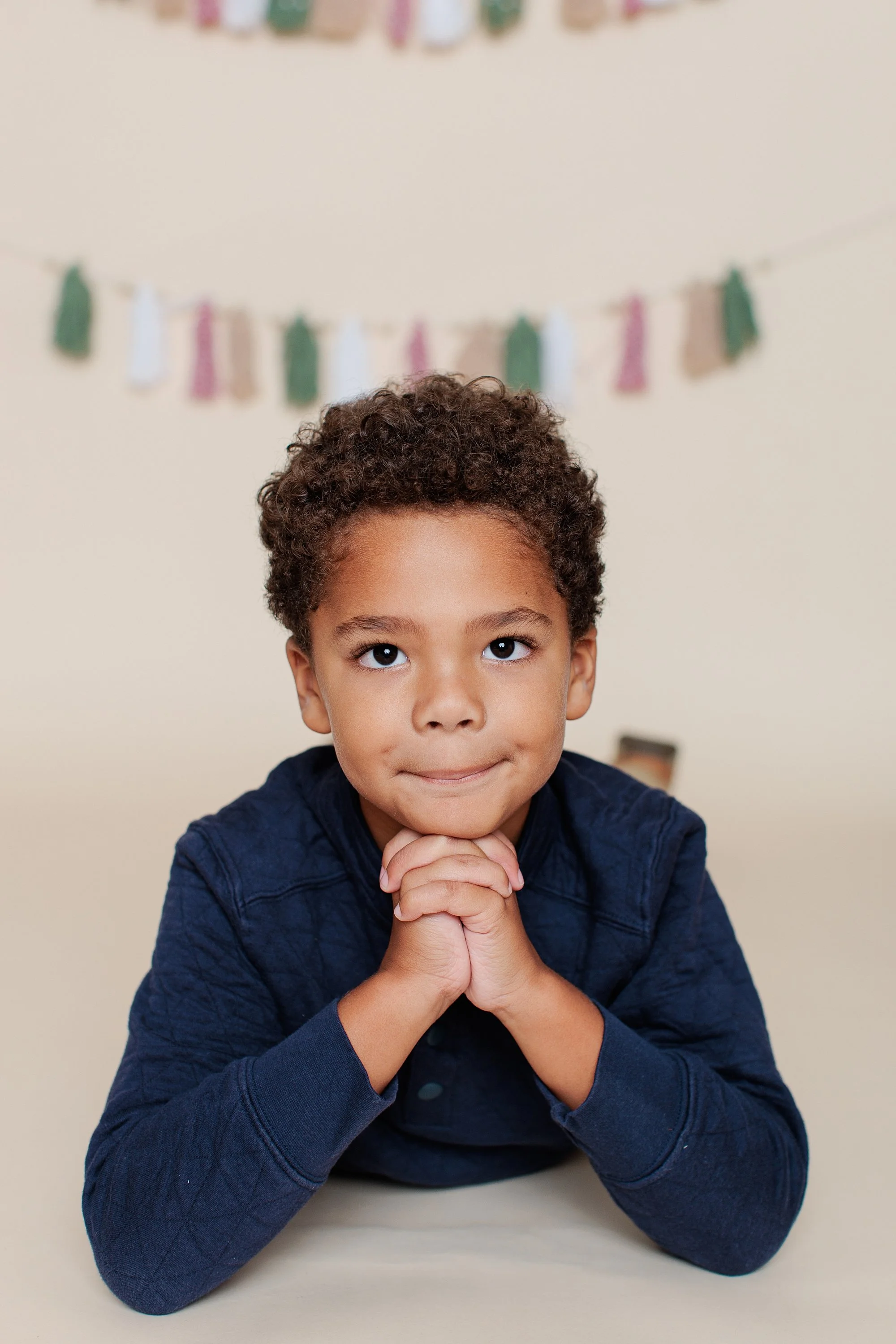 Boy lying on his stomach with his chin on clasped hands, looking upward.
