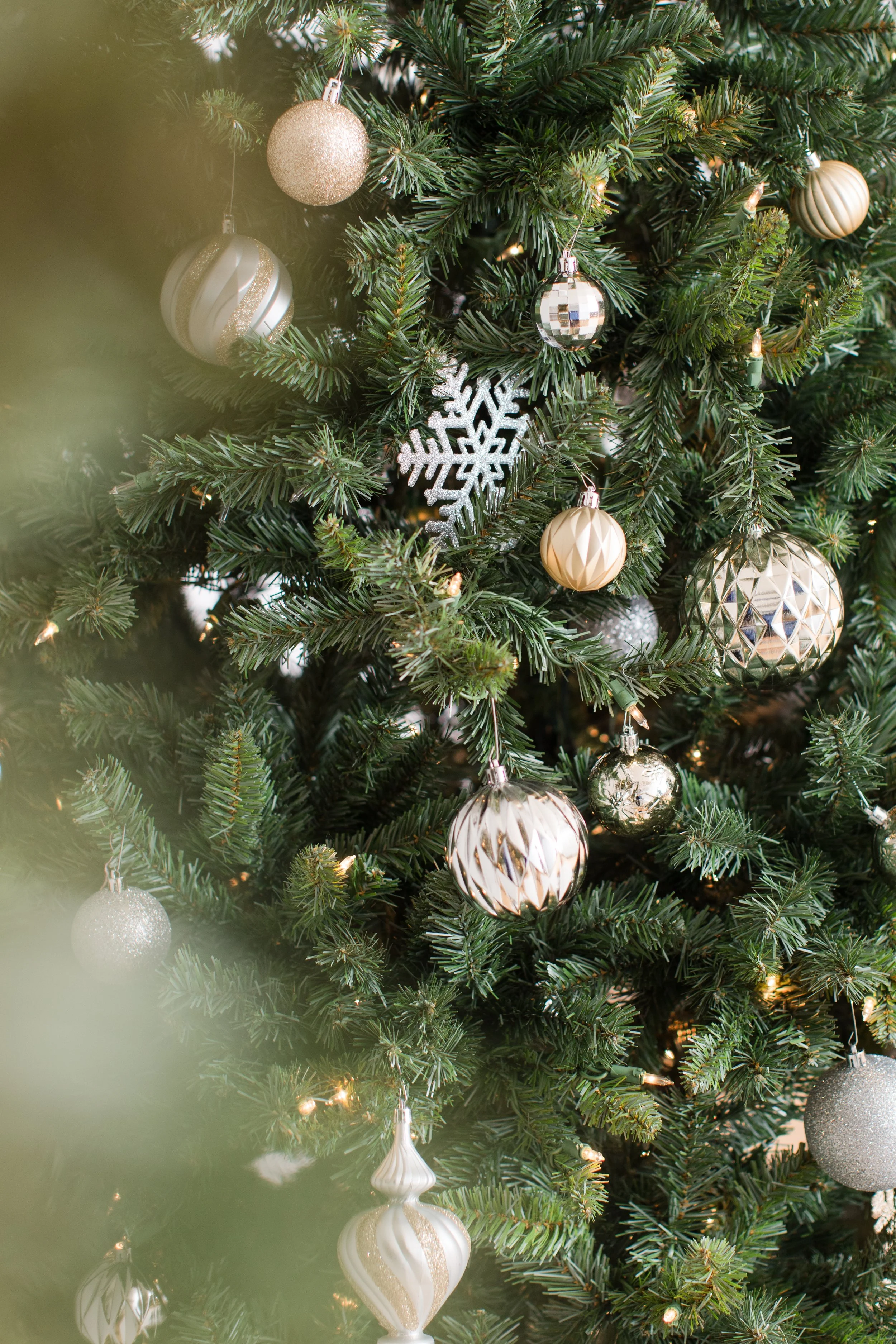 Christmas tree decorated with gold, silver, and white ornaments including baubles, snowflake, and hanging lights.