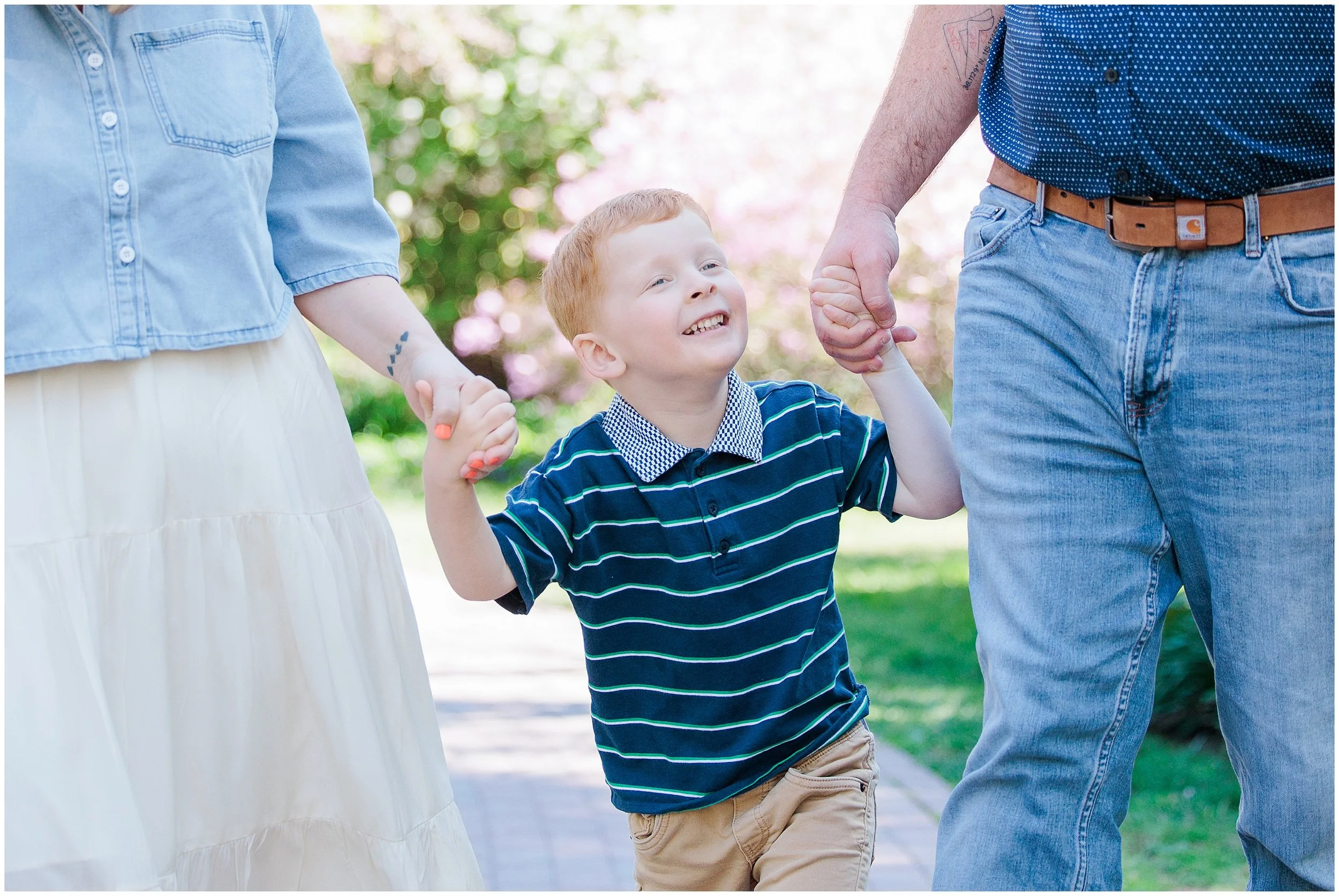 young boy holding parents’ hands and walking along path during spring family photos in Maryland