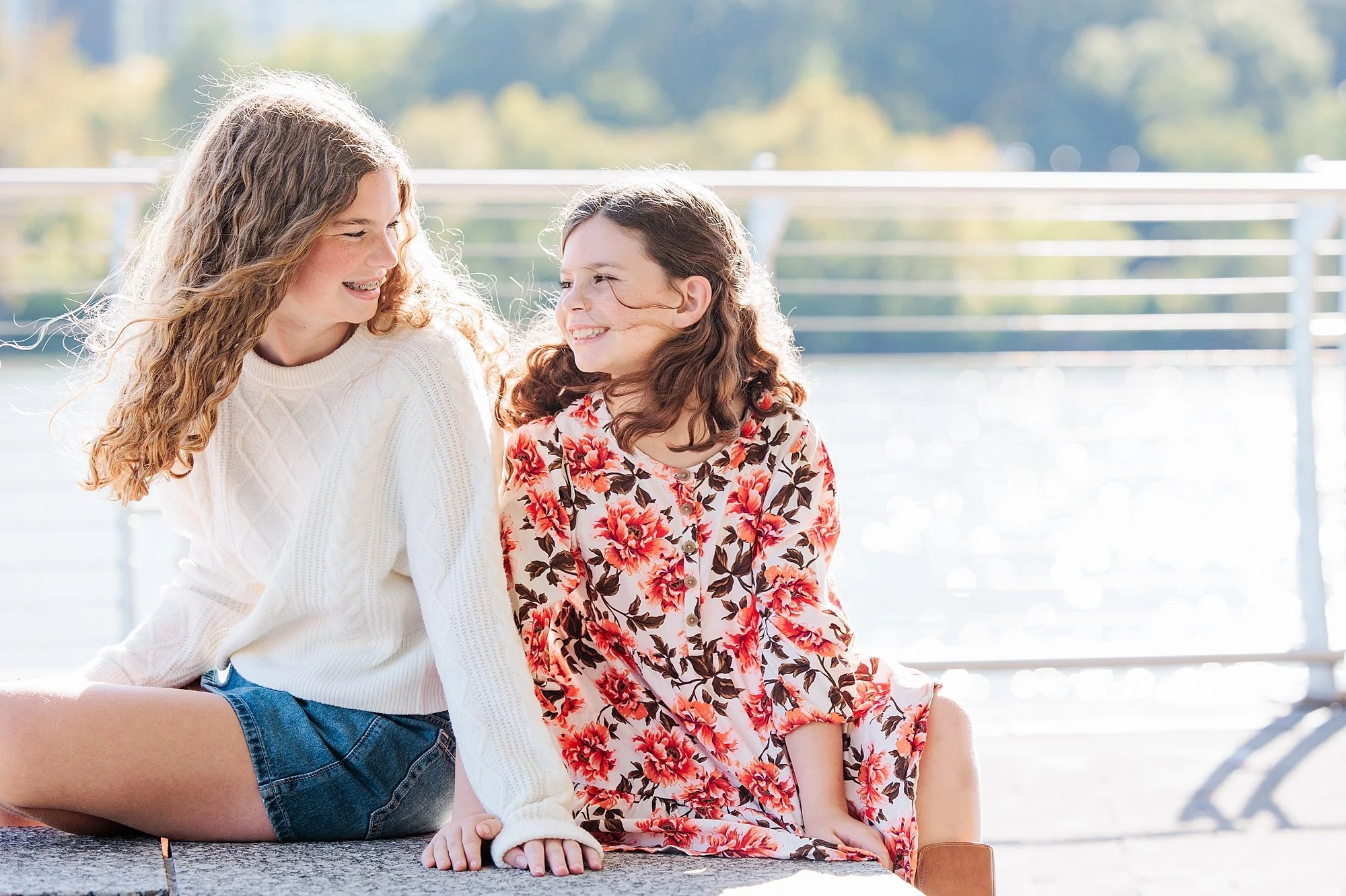 sisters sitting together at Georgetown waterfront for family photos
