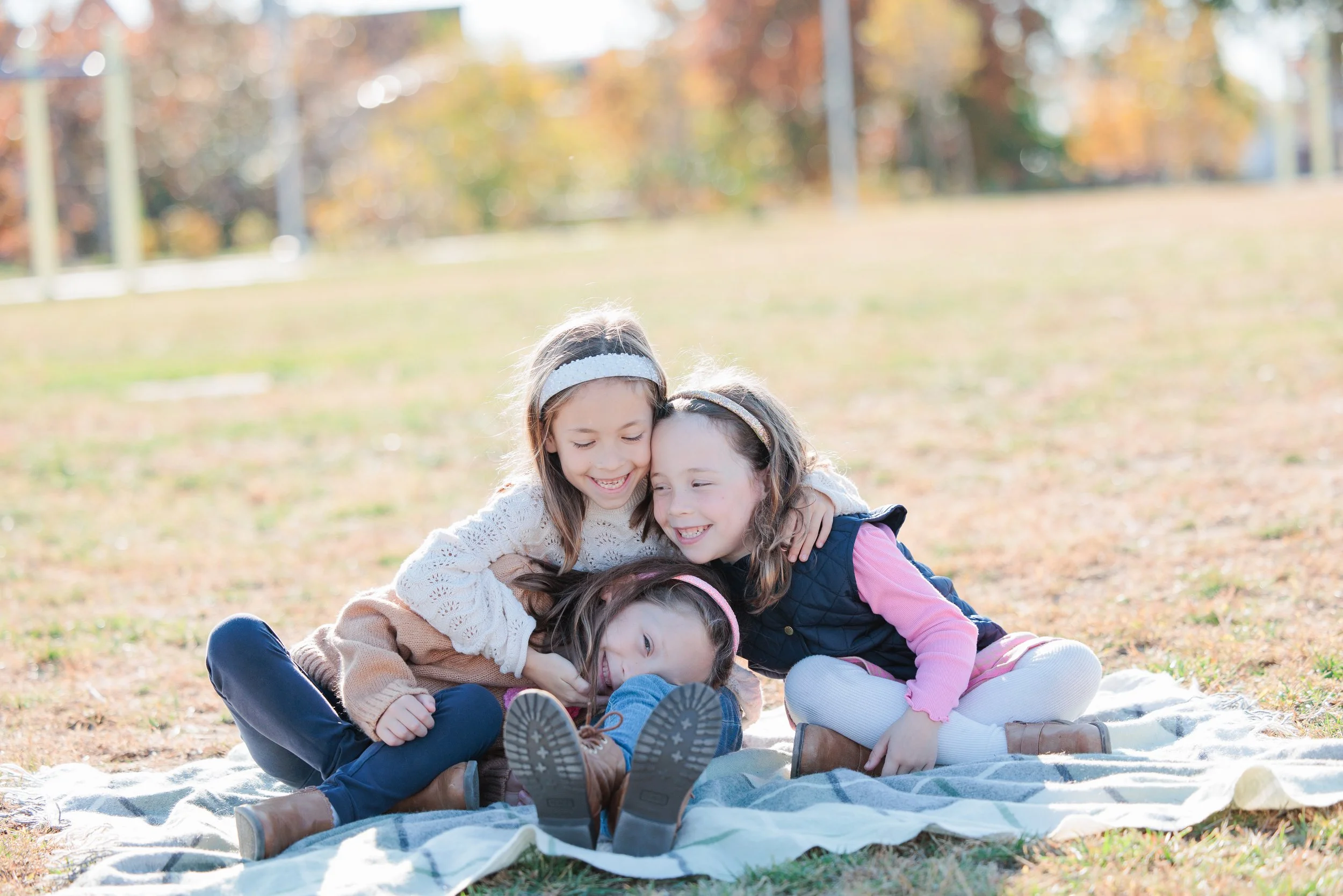 candid moments of three sisters laughing together on a blanket outdoors