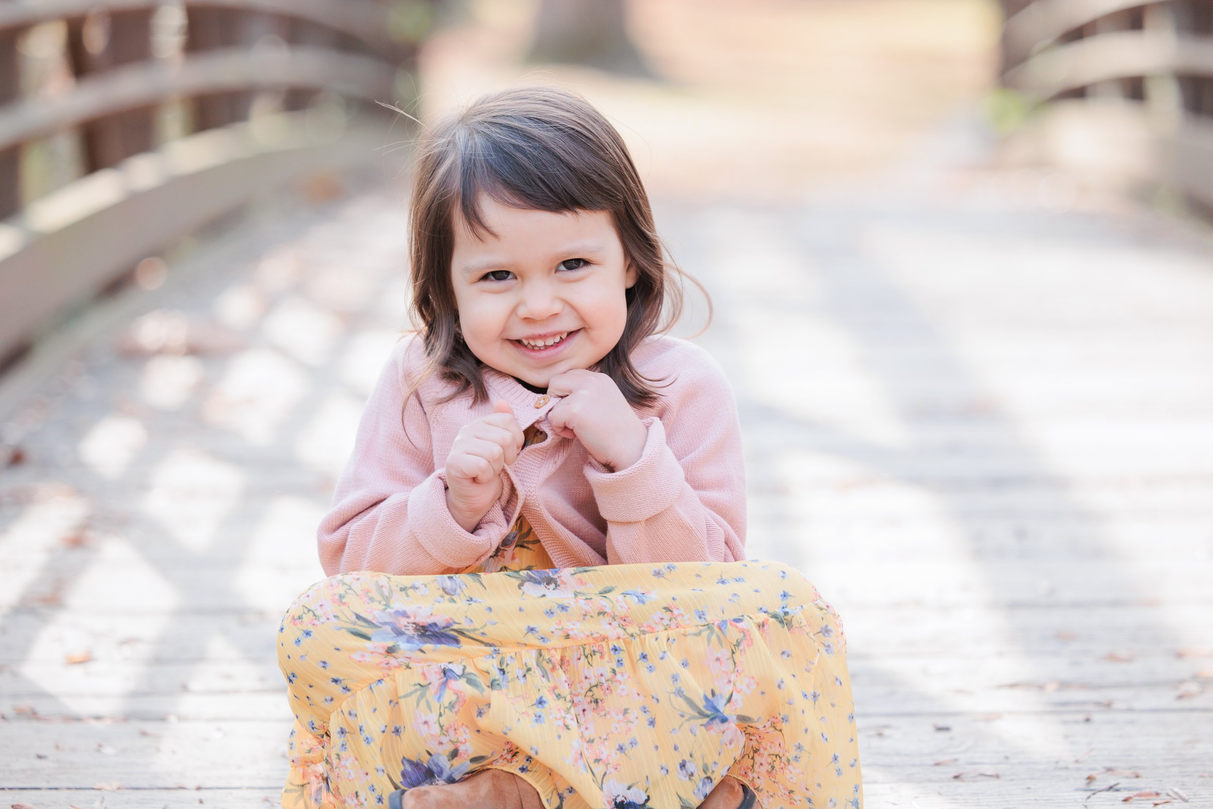 Young girl sitting on a wooden bridge during a soft, natural light family photo session in Maryland
