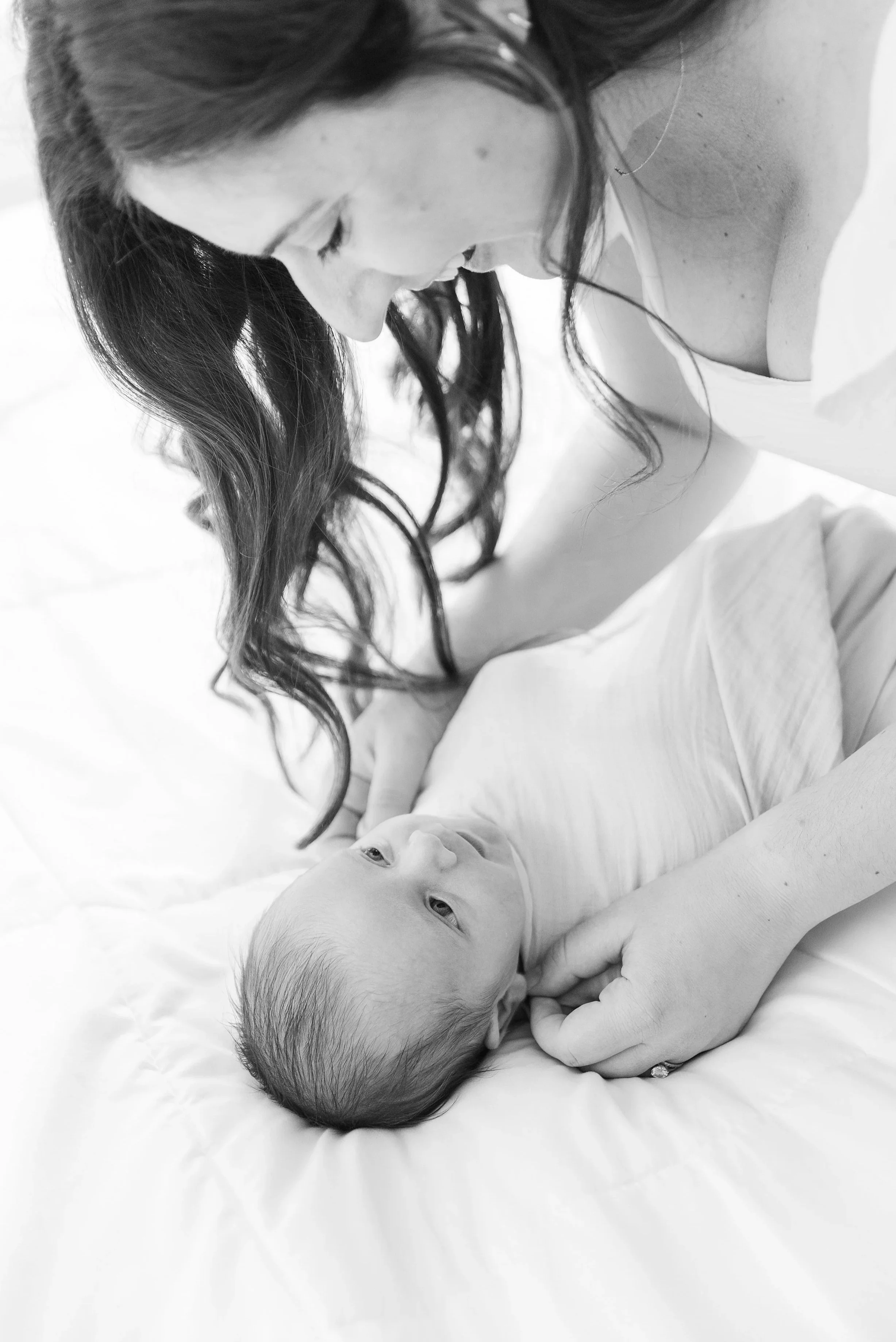 A woman and a baby lying on a bed, with the woman leaning over the baby who is looking up at her.