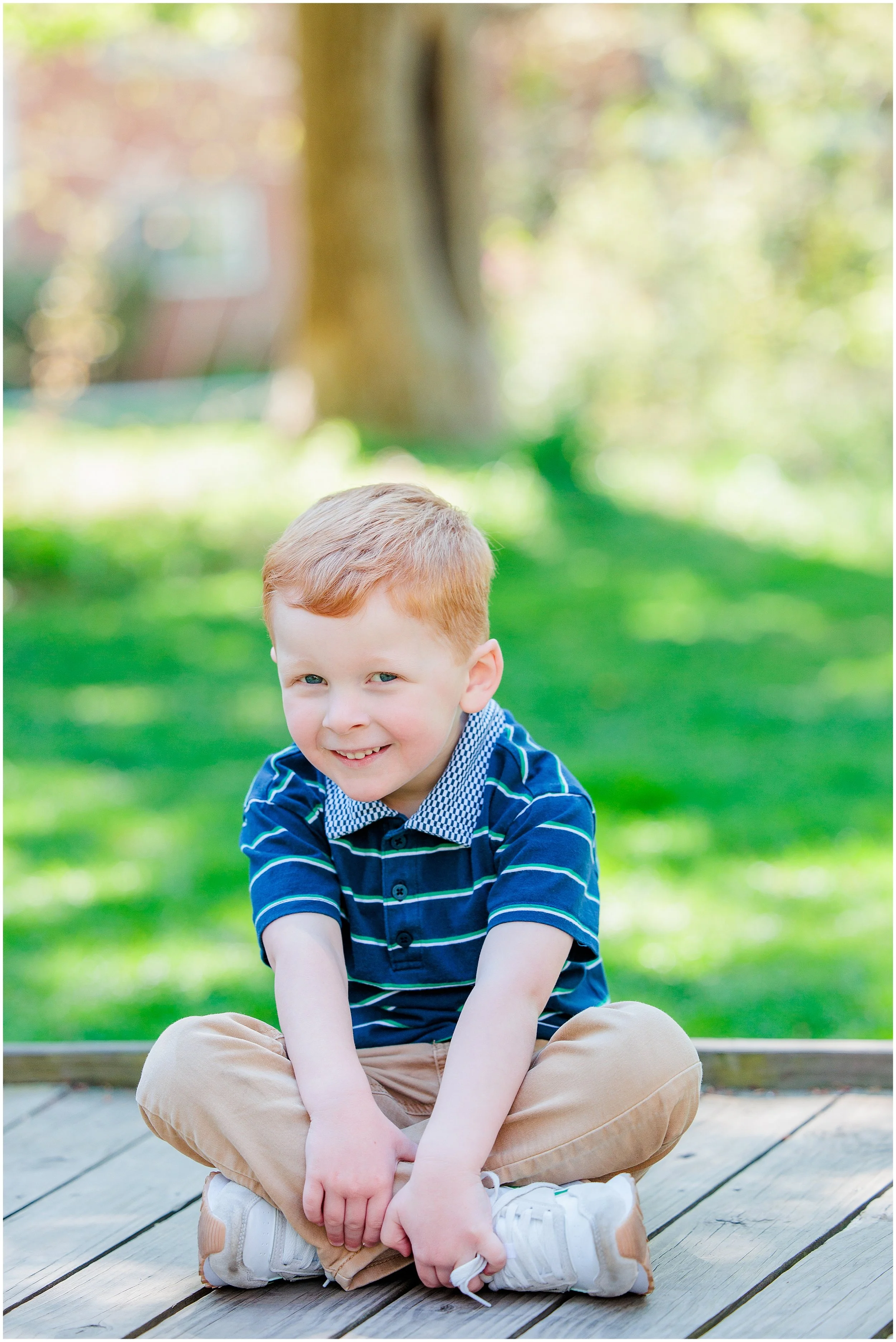 young boy sitting cross-legged and smiling during outdoor spring portrait session in Maryland