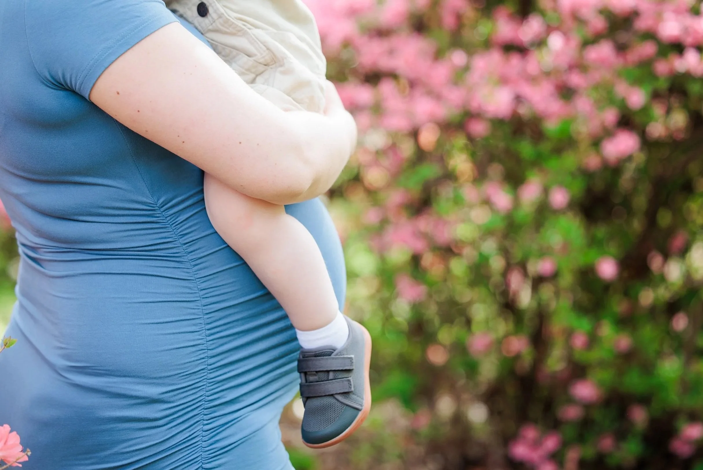 Person carrying a child outdoors with pink flowers in the background.