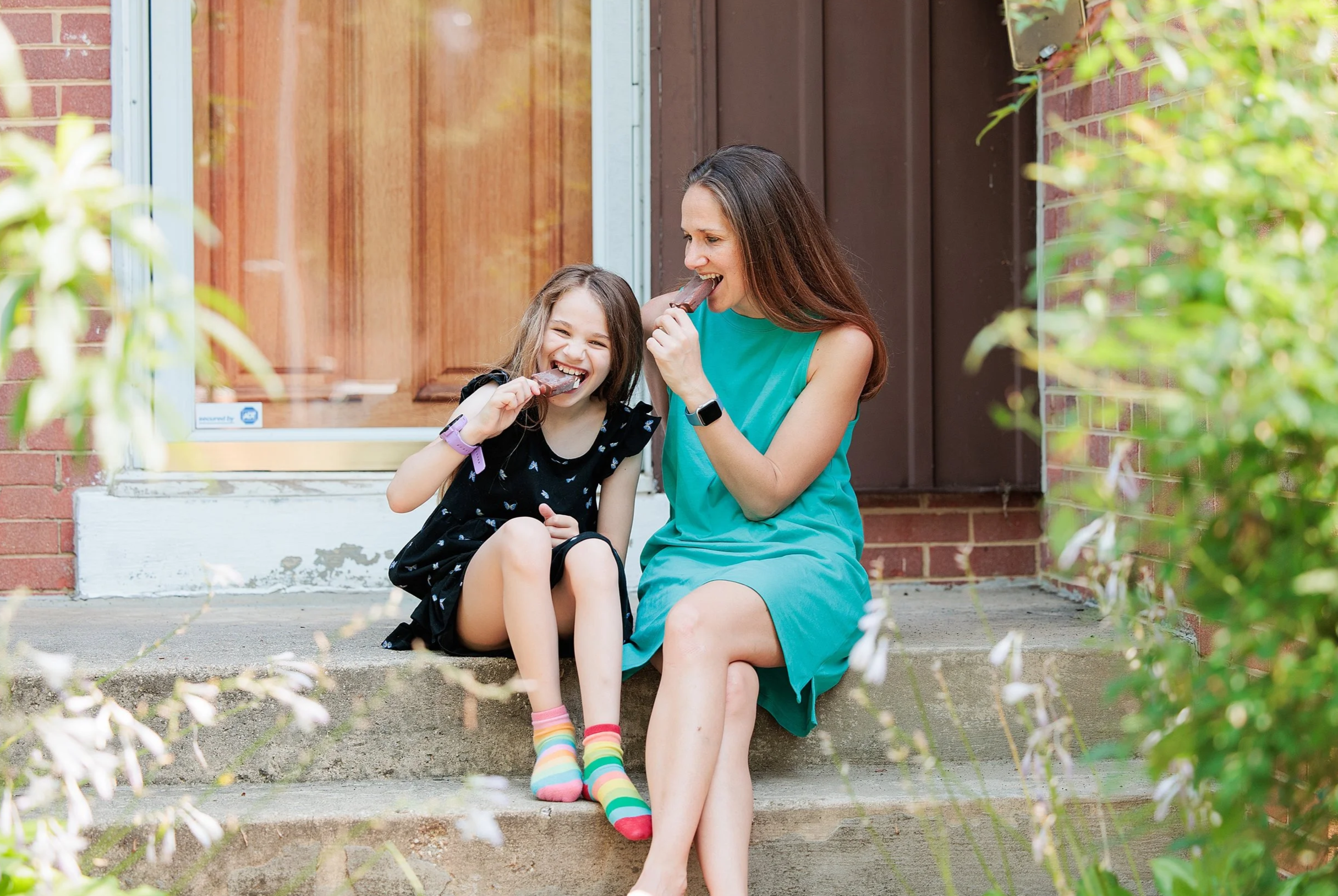 mother and daughter laughing and eating popsicles on porch