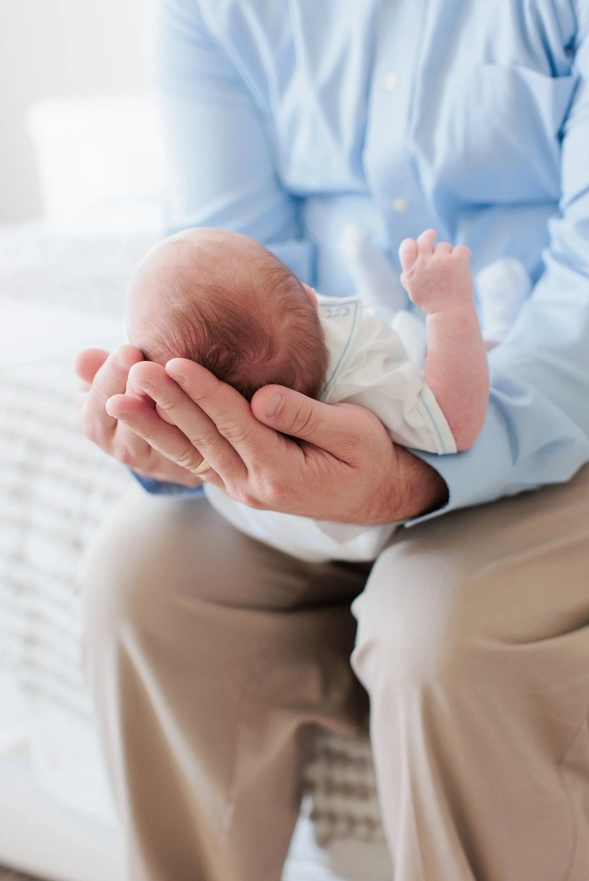 Close-up of a father holding a sleeping baby with a hand supporting the baby's head, scene appears warm and comforting.