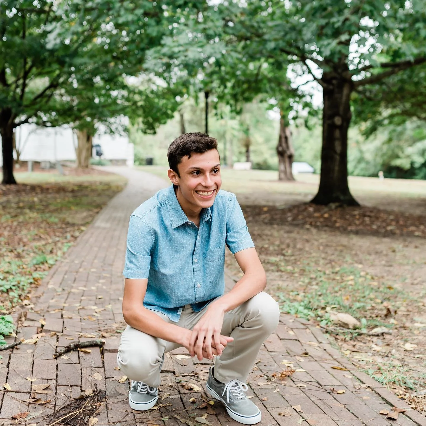 High school senior boy kneeling on brick sidewalk