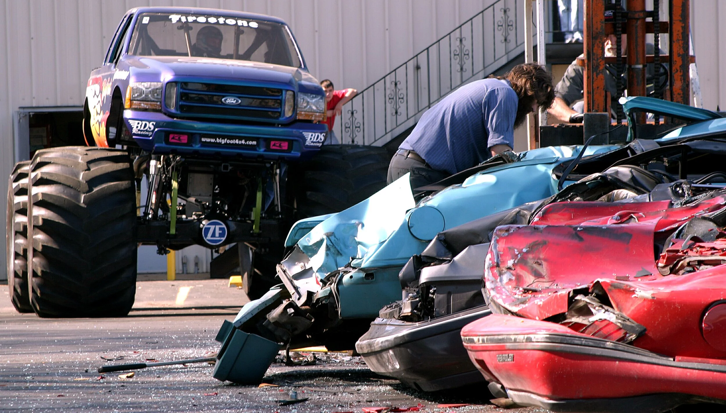  On the flat parking lot, crushed cars try to scurry away after repeated pounding from five tons of monster truck. The shop forklift made a few visits to keep everything in place. 