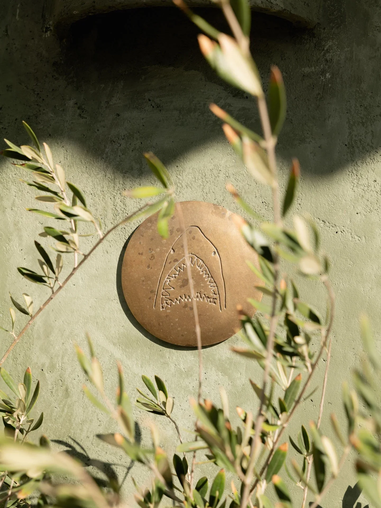 The mark of the coast. Our iconic brass shark logo embedded in the plaster walls at Great White Restaurant Venice, symbolizing our roots in Australian surf culture.