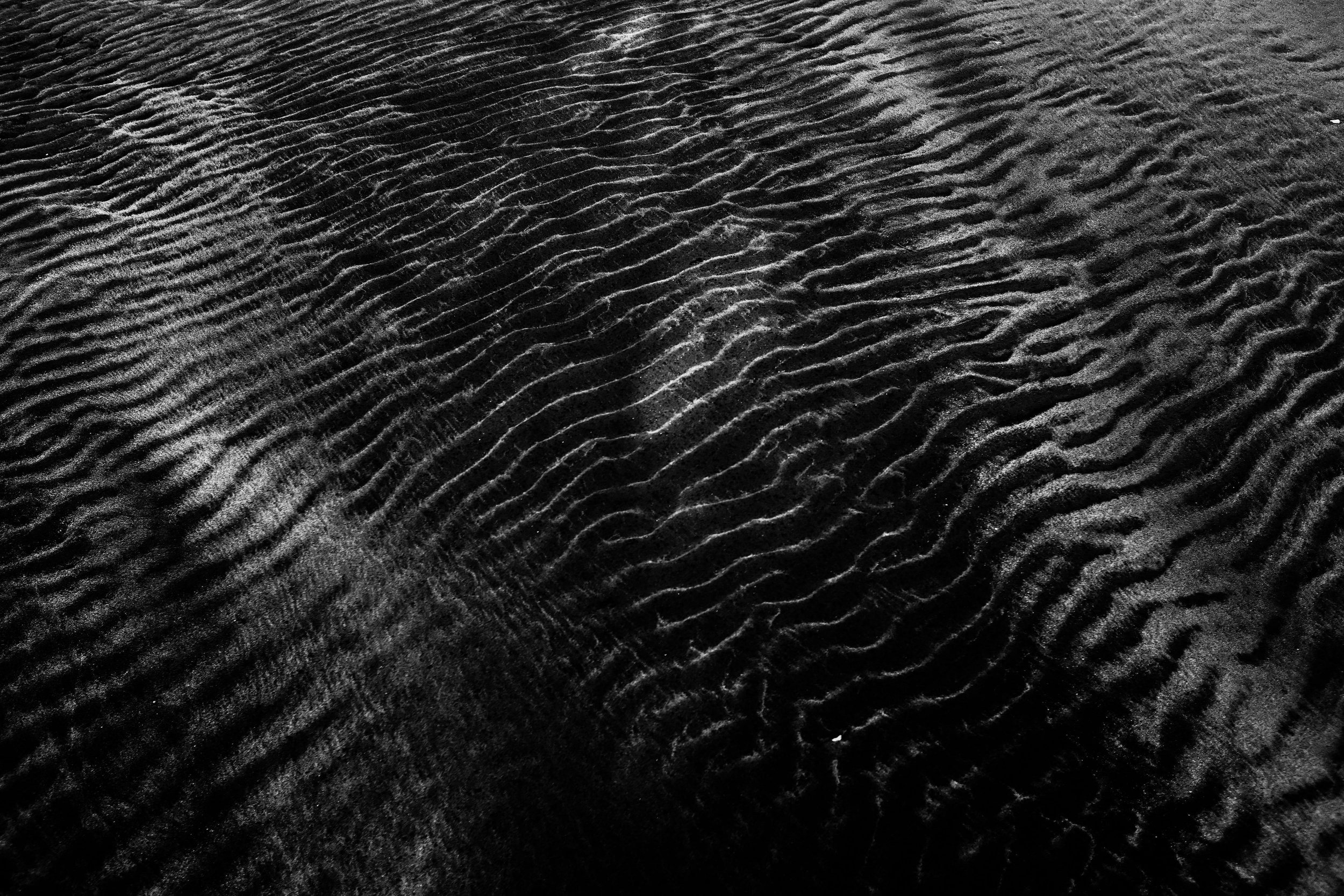 Black sand with ripples and textured patterns.