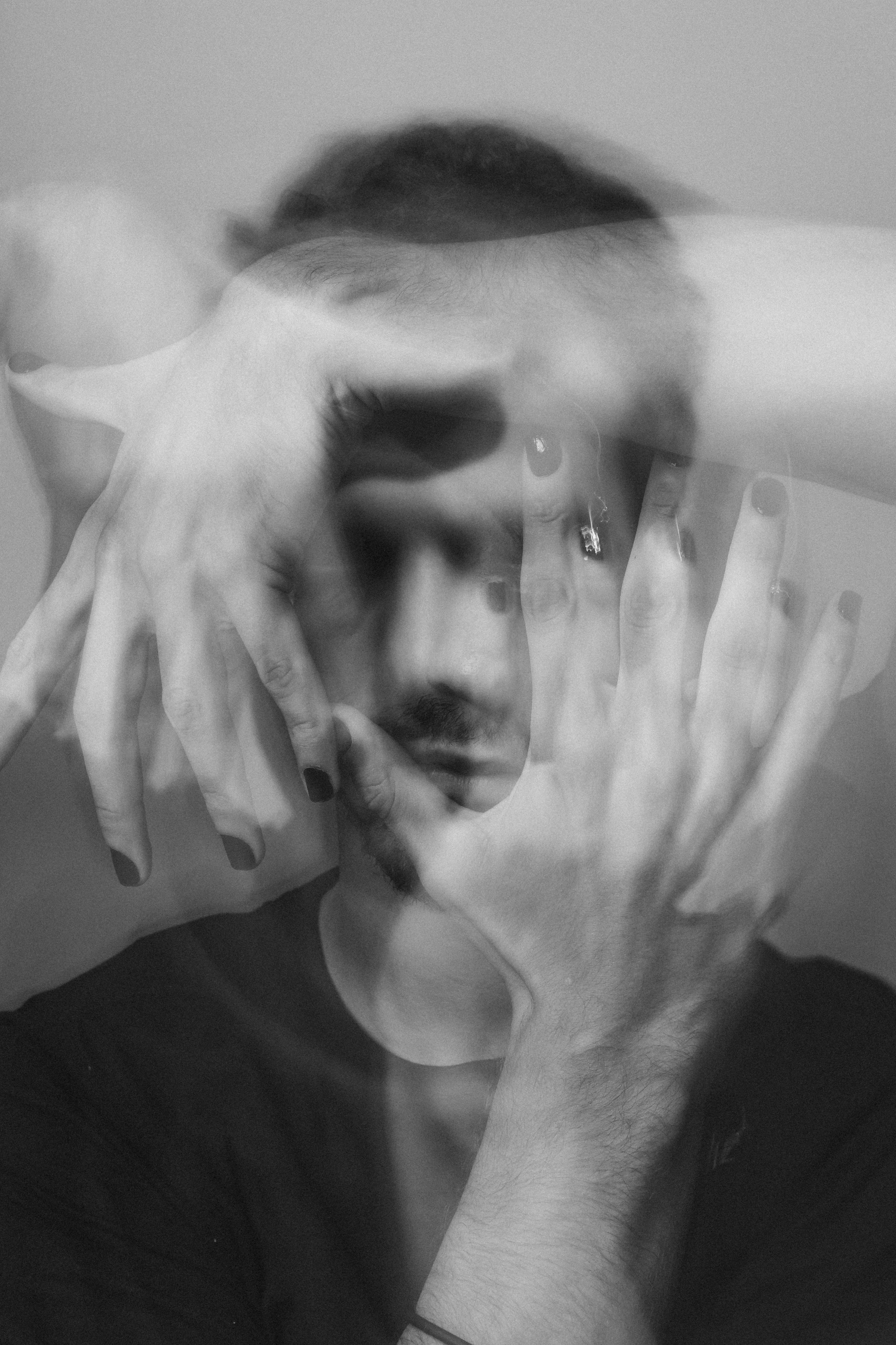 A black-and-white photo of a person with hazy, overlapping hands and face, creating a layered, abstract effect.