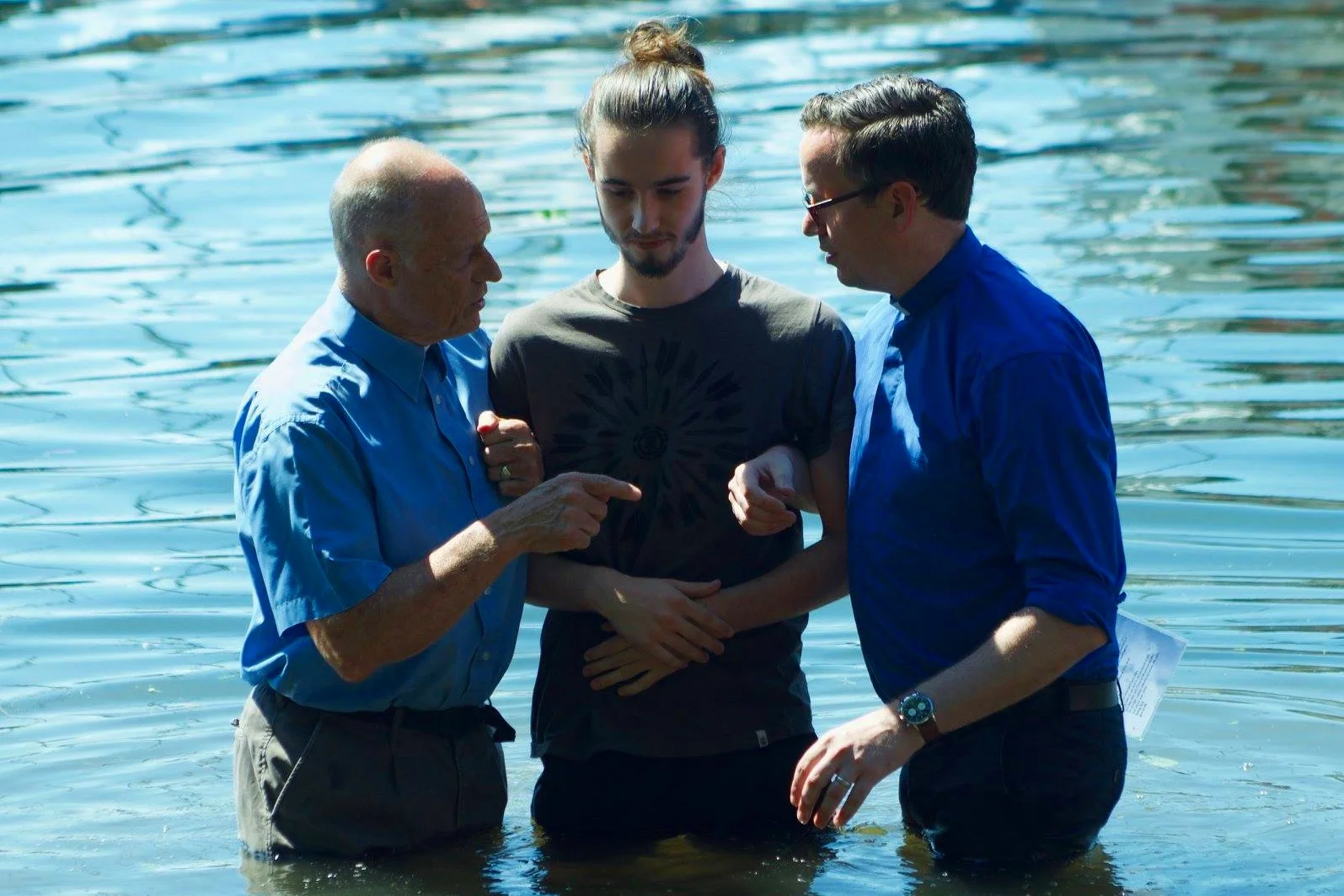A photograph of a young man being baptised by the vicar in the River Thames
