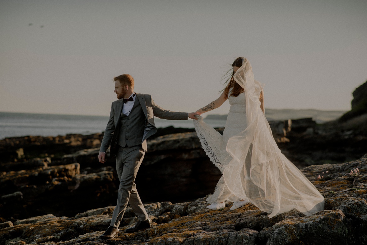 bride and groom are walking on beach