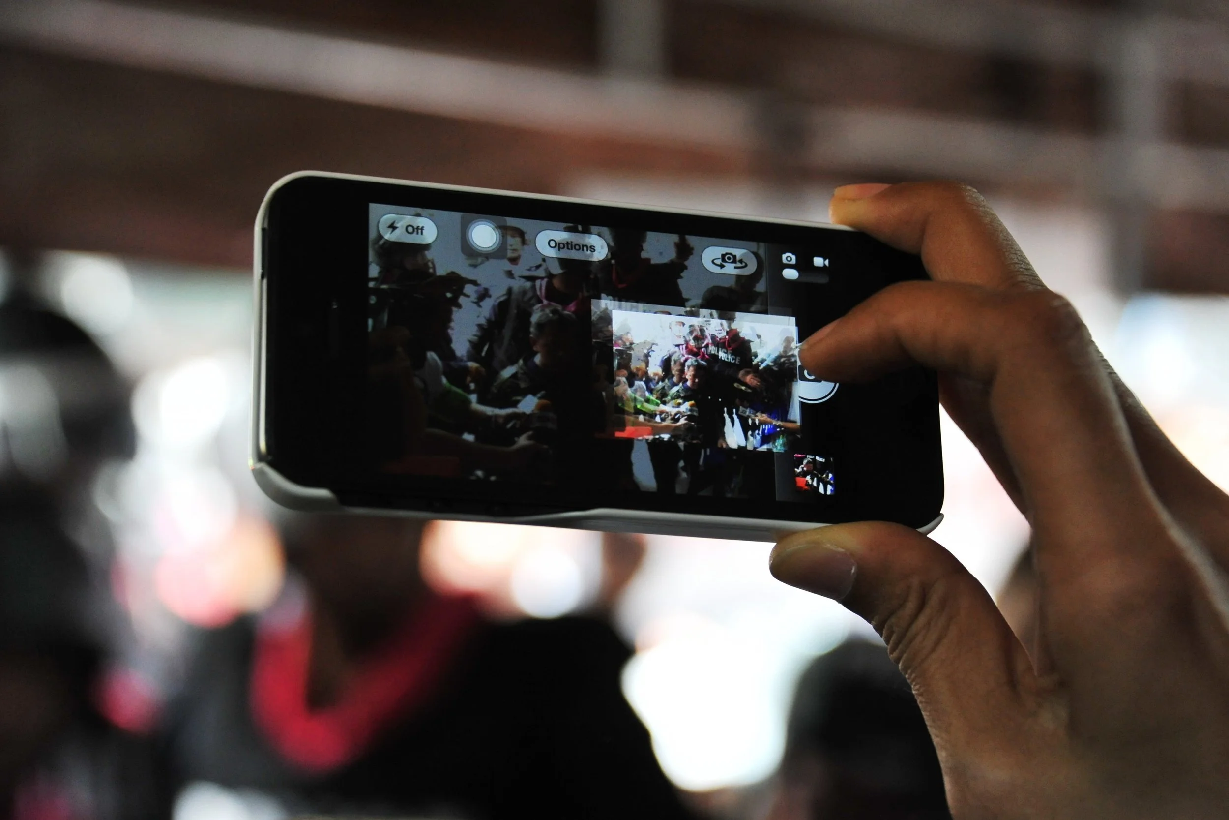 A close up shot on a hand holding a cell phone as the owner films police officers.