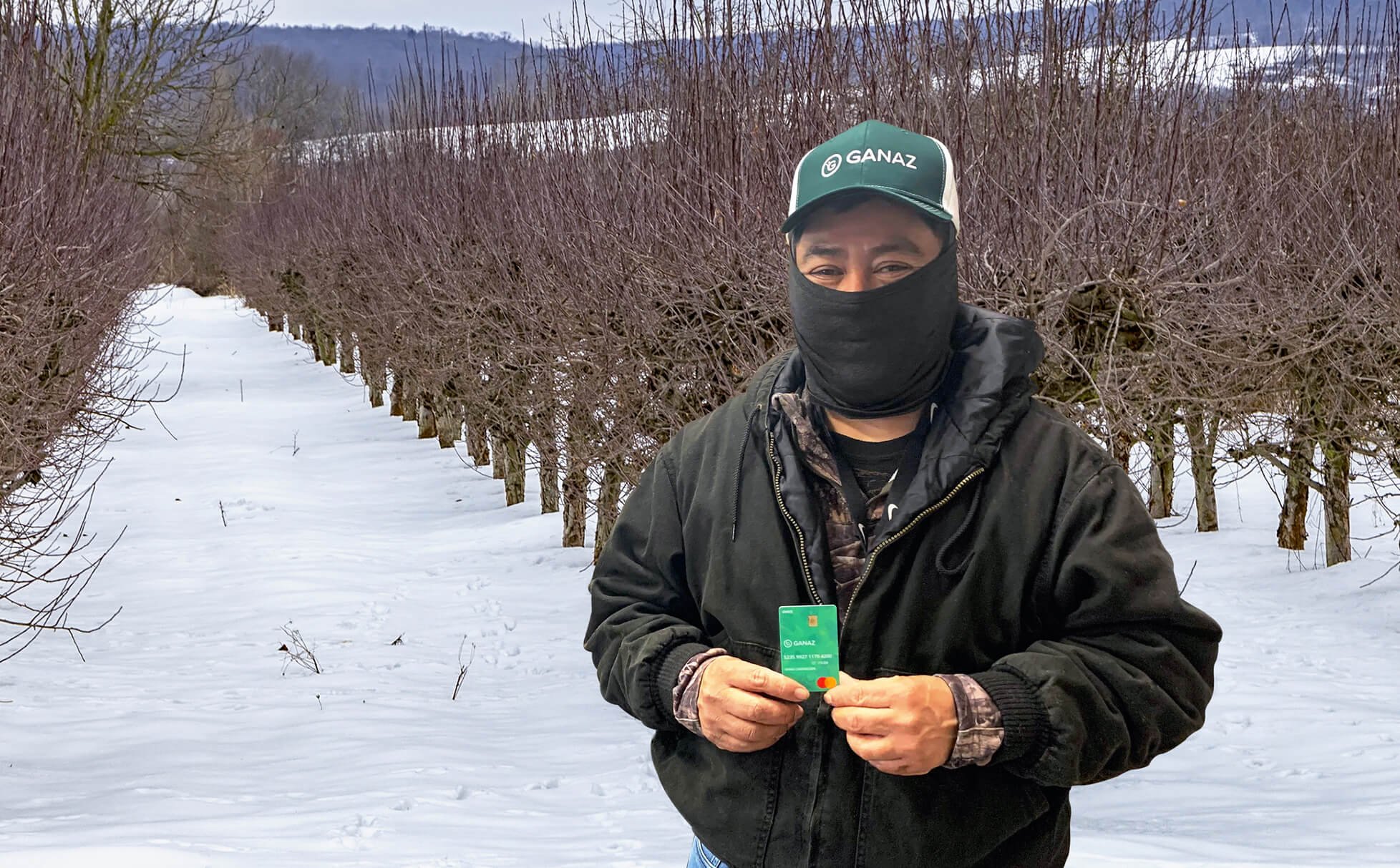 Mauricio holding a Ganaz Payroll Card in an apply orchard in winter