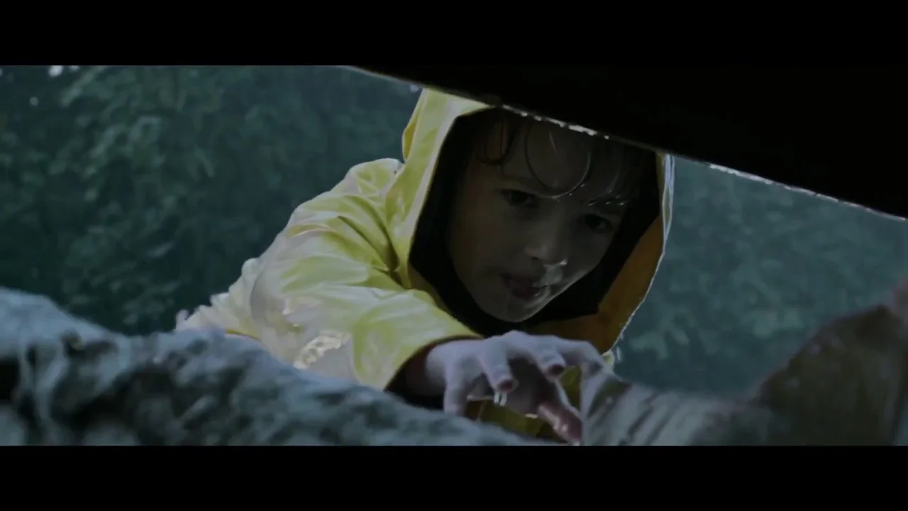 Jackson Robert Scott, as Georgie Denbrough, reaches into the sewer to retrieve his paper boat from Pennywise the Dancing Clown in It