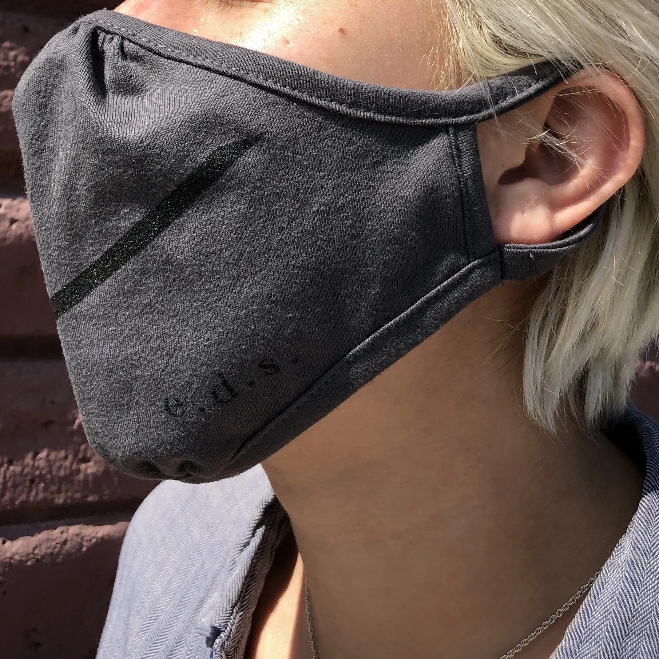 EDS Face Mask in a Dark Grey with Black Diagonal Stripe across the mask, and ‘e.d.s.’ prited on the lower left side of the mask. 