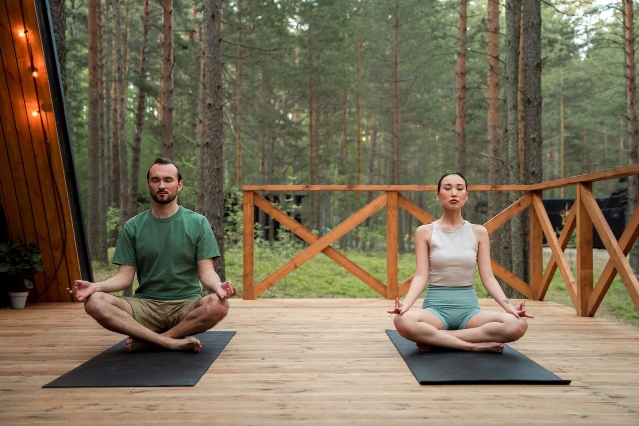 A man and a woman meditating in lotus position on a wooden deck